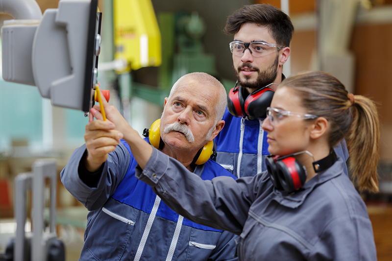 photo of a senior engineer explaining machinery to male and female apprentices